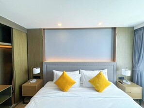 Habitación de hotel con una cama grande, dos lámparas de noche, un armario de madera y un cabecero de color neutro.