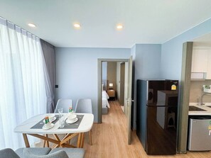 Una habitación de hotel compacta con comedor, cama, kitchenette y baño.