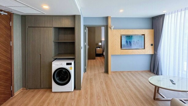 A compact hotel room with a washing machine, a flat-screen TV mounted on the wall, and a round table. - Suite Solis 2br | Resort pool view | 300m to rawai (Rawai)