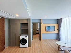 Habitación de hotel compacta con lavadora, televisor de pantalla plana montado en la pared y una mesa redonda.