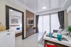 Habitación de hotel con cama, televisión, escritorio con silla y mesa de comedor con un jarrón de flores.