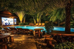 A poolside area with lounge chairs, wooden tables, and a bar area with illuminated artwork. - Nova Condo 1br | Pool view | nbc nai harn (Rawai)