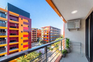 A balcony with a view of colorful apartment buildings, a metal railing, and a potted plant. - Nova Condo 1br | Pool view | nbc nai harn (Rawai)