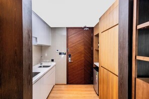 A narrow kitchen with a wooden door, white cabinets, and a stainless steel sink.