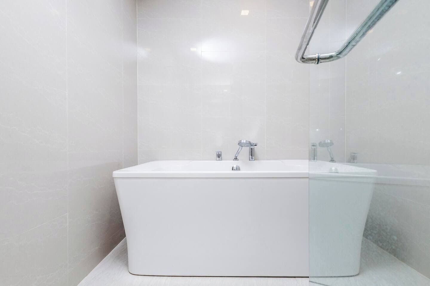 Ein modernes Badezimmer mit einer großen weißen Badewanne, einer Duschbrause und einer gläsernen Duschkabine.