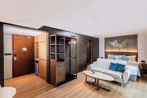 A modern hotel room with a wooden wardrobe, a sofa bed, a coffee table, and a decorative wall piece. - Studio Aurel 1br|tropical Views|shuttle to Naiharn (Rawai)