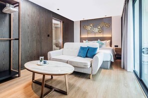 A modern hotel room with a sofa, a round table, a bed with a headboard, and a decorative wall piece.