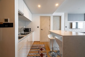 A modern kitchen with a built-in microwave, sink, and a bar area with stools. - Duplex Cala 1br | Family|pools|gym & shuttle (Rawai)