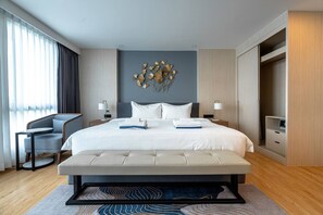 Une chambre d’hôtel moderne avec un grand lit, deux tables de chevet, une chaise, un élément décoratif mural et une armoire.