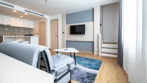 Een moderne hotelkamer met een bed, een klein tafeltje, een televisie, een keukenhoek en een trap.