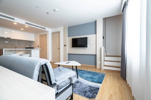 A modern hotel room with a bed, a small table, a TV, a kitchen area, and a staircase. - Duplex Cala 1br | Family|pools|gym & shuttle (Rawai)