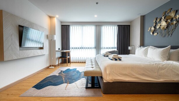 Een moderne hotelkamer met een groot bed, een flatscreen televisie aan de muur, een bureau met stoel, en een groot raam met gordijnen.