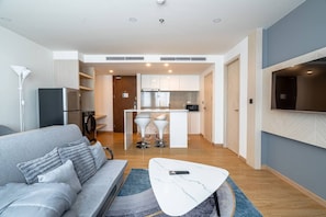 A modern living room with a grey sofa, a white coffee table, and a TV mounted on the wall. - Duplex Cala 1br | Family|pools|gym & shuttle (Rawai)