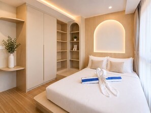 A modern hotel room with a large bed, a built-in wardrobe, and a bedside table with a vase of flowers.