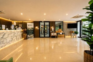 A hotel reception area with a marble counter, a reception desk, a large poster, and a reception desk with a computer and a plant.