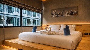 A modern hotel room with a large bed, a cityscape view, and a wooden floor. - Studio Aira| Rooftop Pool | relife naiharn beach (Karon)