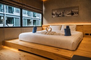 A modern hotel room with a large bed, a cityscape view, and a wooden floor.