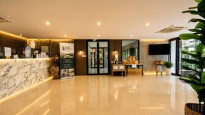 A hotel reception area with a marble counter, a reception desk, a large poster, and a reception desk with a computer and a plant. - Studio Aira| Rooftop Pool | relife naiharn beach (Karon)