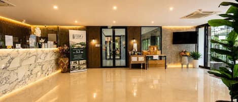 A hotel reception area with a marble counter, a reception desk, a large poster, and a reception desk with a computer and a plant.