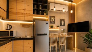 A modern kitchen with wooden cabinets, a stainless steel refrigerator, a microwave, and a dining area with wooden chairs and a table. - Studio Aira| Rooftop Pool | relife naiharn beach (Karon)