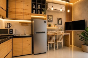 A modern kitchen with wooden cabinets, a stainless steel refrigerator, a microwave, and a dining area with wooden chairs and a table.