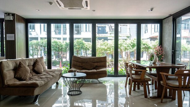 A modern interior with a sofa, armchair, dining table, and chairs, large windows offering a view of the outdoors. - Studio Aira| Rooftop Pool | relife naiharn beach (Karon)