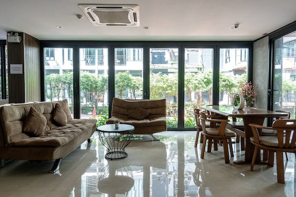 A modern interior with a sofa, armchair, dining table, and chairs, large windows offering a view of the outdoors.