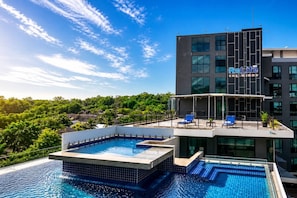 A modern building with a rooftop pool and lounge area, surrounded by greenery.