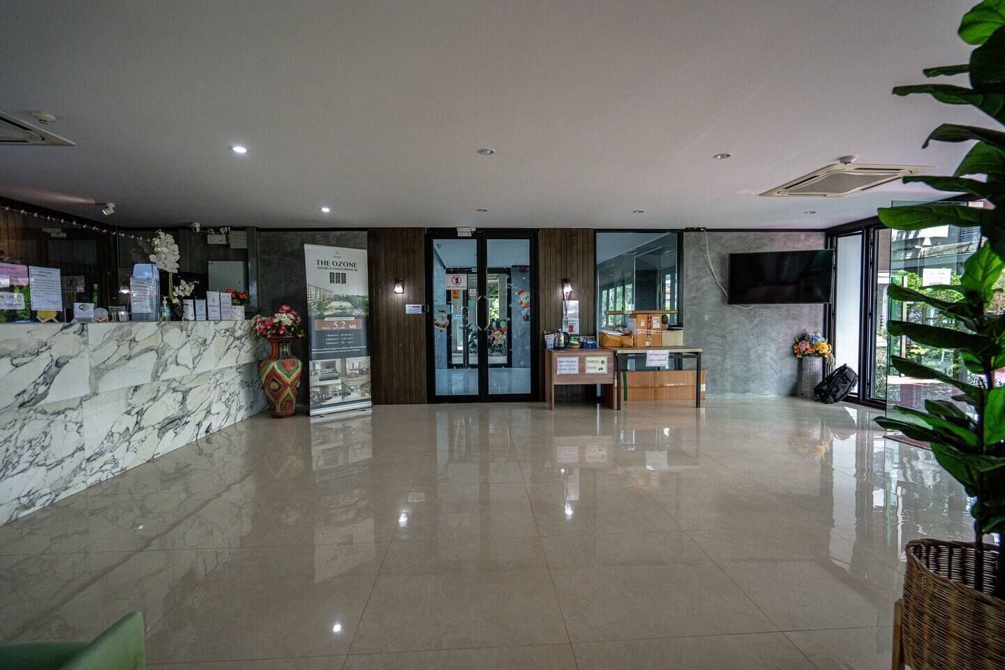 Un vestíbulo de hotel con un mostrador de recepción de mármol, un área de recepción con una computadora y una pequeña mesa, y un ventanal que ofrece vistas al exterior.