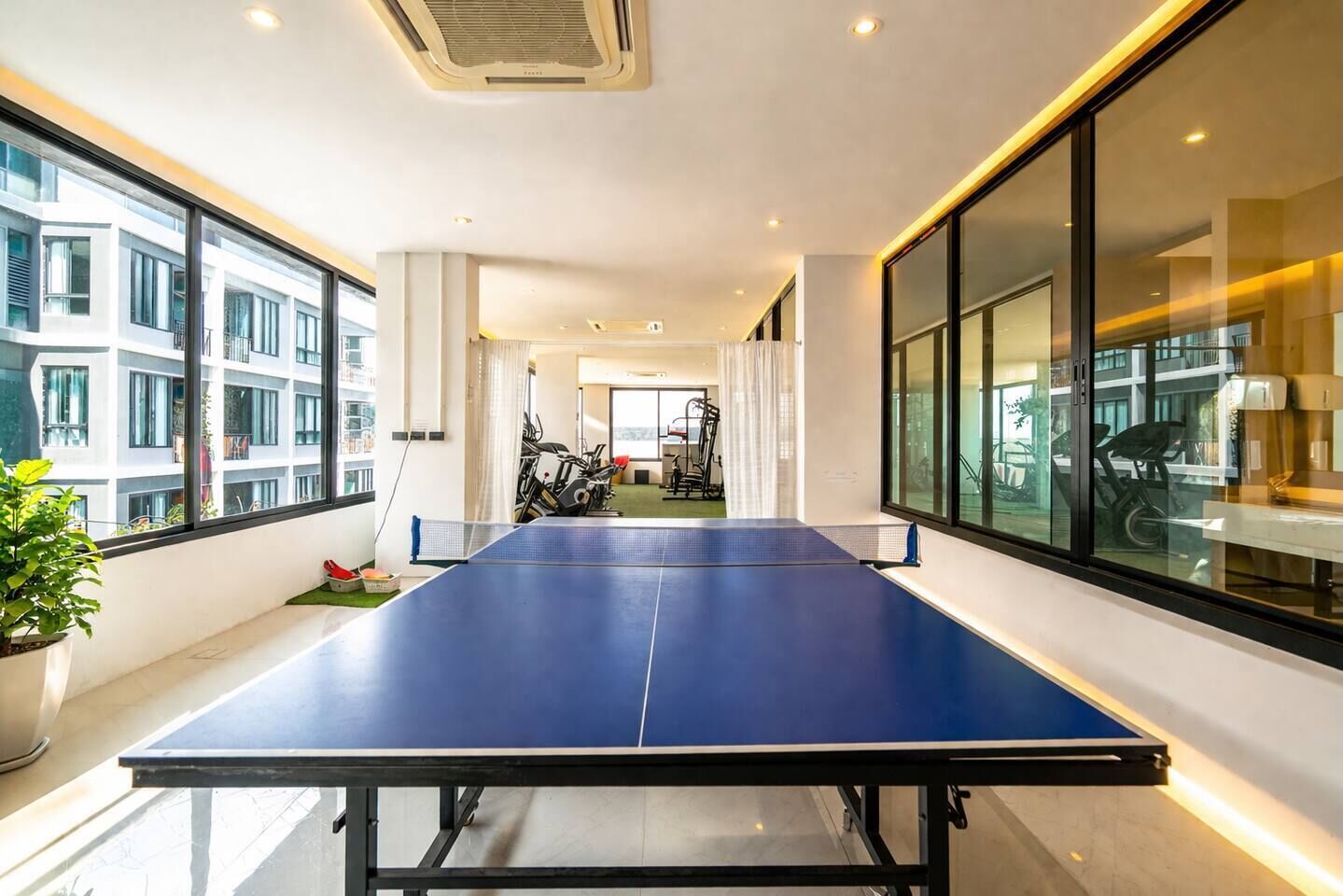 Amplia habitación con mesa de ping pong, ventanas grandes y equipo de ejercicio.