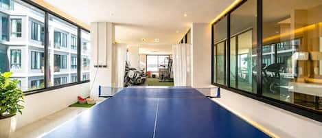 Amplia habitación con mesa de ping pong, ventanas grandes y equipo de ejercicio.