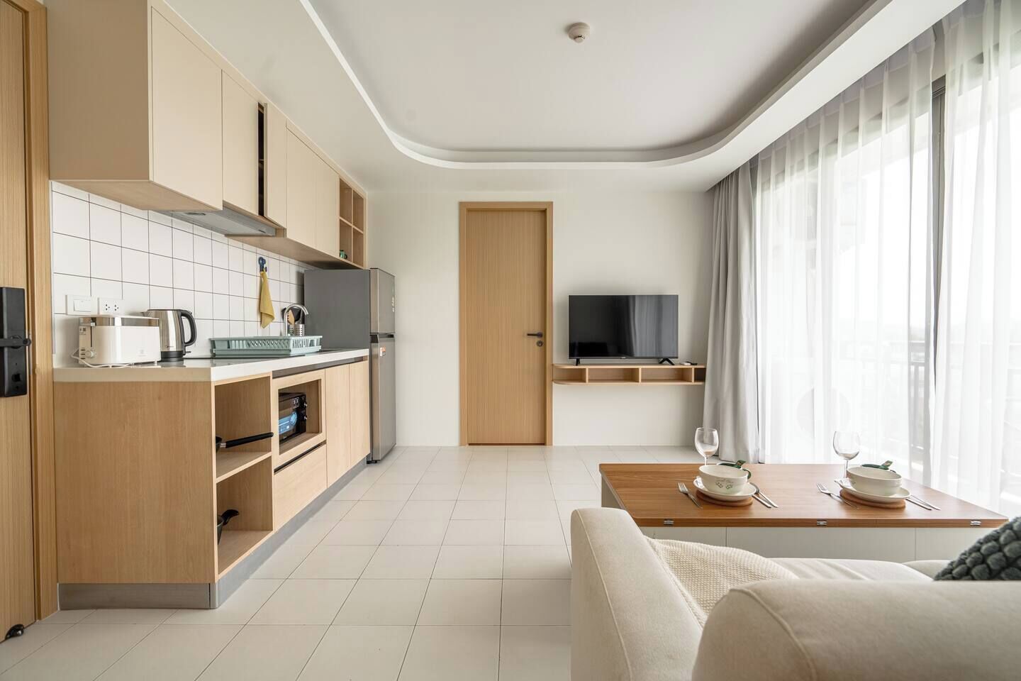 Una cocina moderna con electrodomésticos integrados, un comedor con mesa dispuesta para dos personas y un televisor montado en la pared.