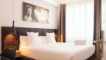 A hotel room with a large bed, a headboard, a bedside table, a lamp, a painting on the wall, and a window with curtains.