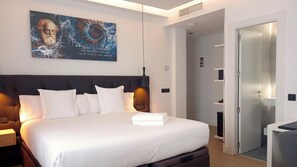 Un lit bien fait, avec du linge de lit blanc, une tête de lit sombre et une œuvre d’art accrochée au mur.