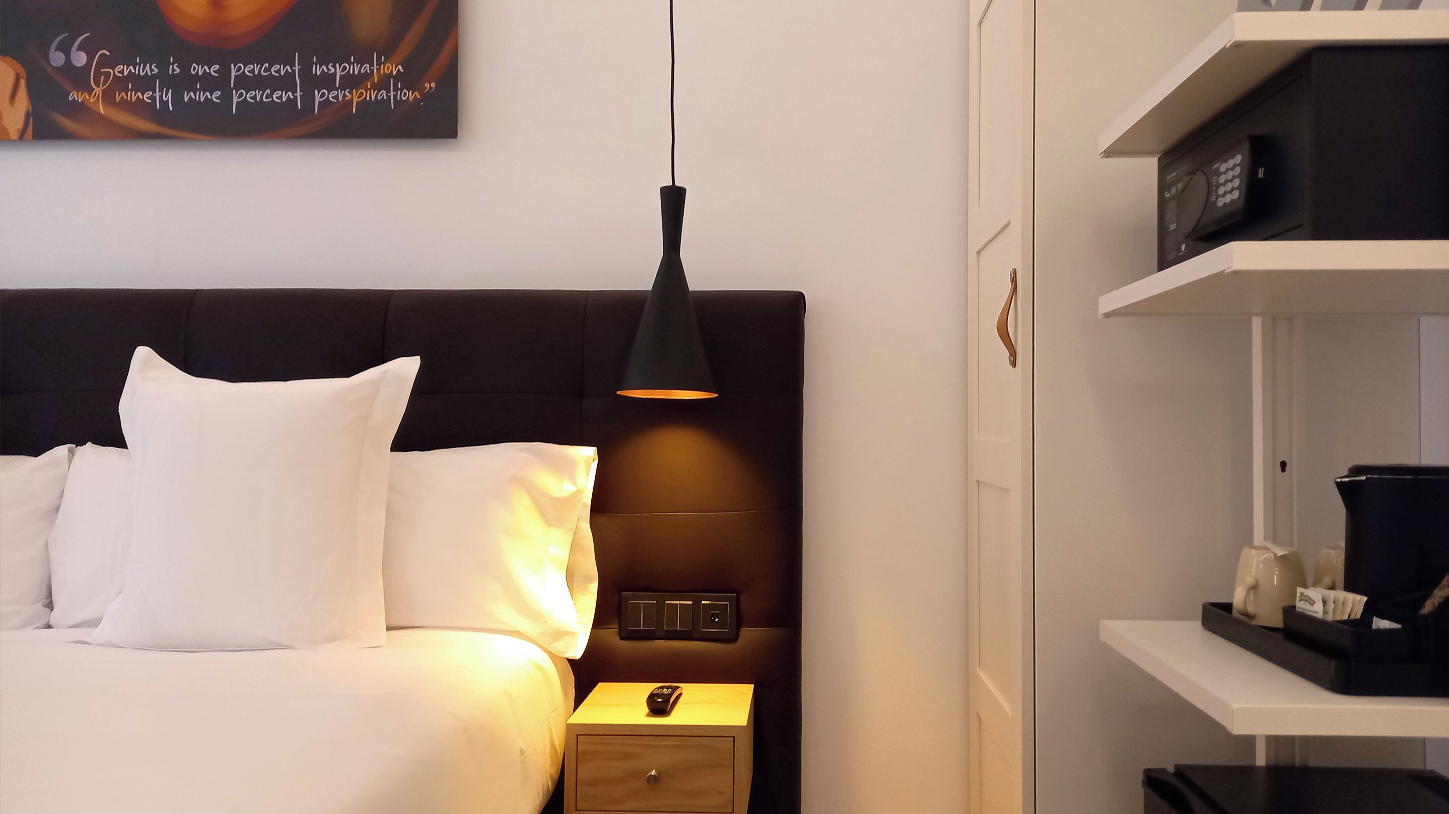 A modern bedroom with a bed, bedside table, lamp, and a shelf with items.