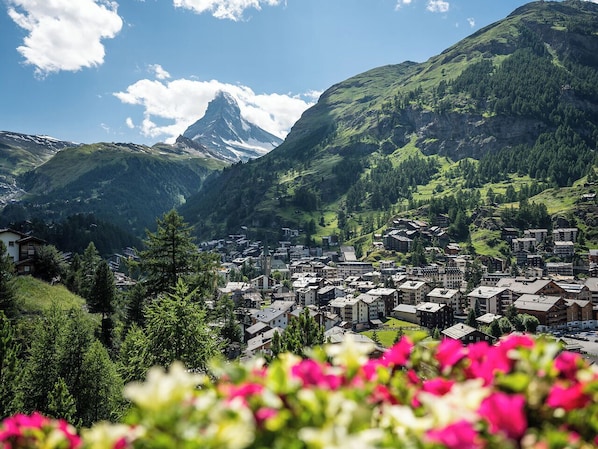 A mountain town with buildings, a prominent church, and lush greenery. - Charming Alpin Violett (Zermatt)