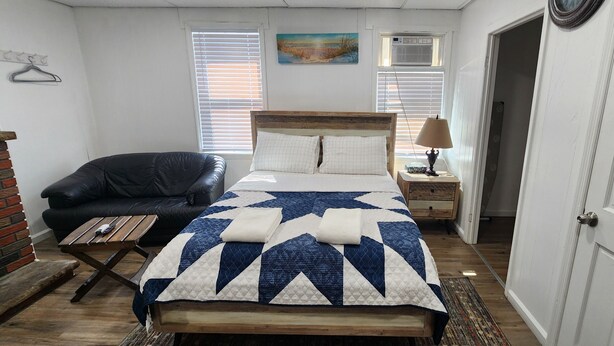 Un dormitorio con una cama, una silla, una mesita de noche y una lámpara.