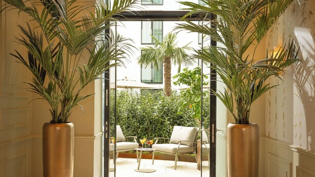A hallway with a checkered floor, large potted plants, and a view of an outdoor seating area. - EST Hotel Palais Chotek NEW OPENING (Vienna)