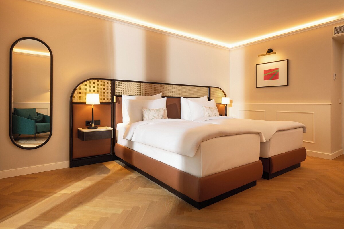 A double bed with a wooden frame, two bedside tables with lamps, a mirror, and a framed picture on the wall.