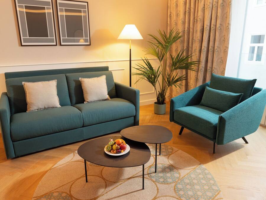 Una sala de estar con un sofá color turquesa, un sillón a juego, una mesita de centro con fruta, una lámpara de pie y una planta en maceta.
