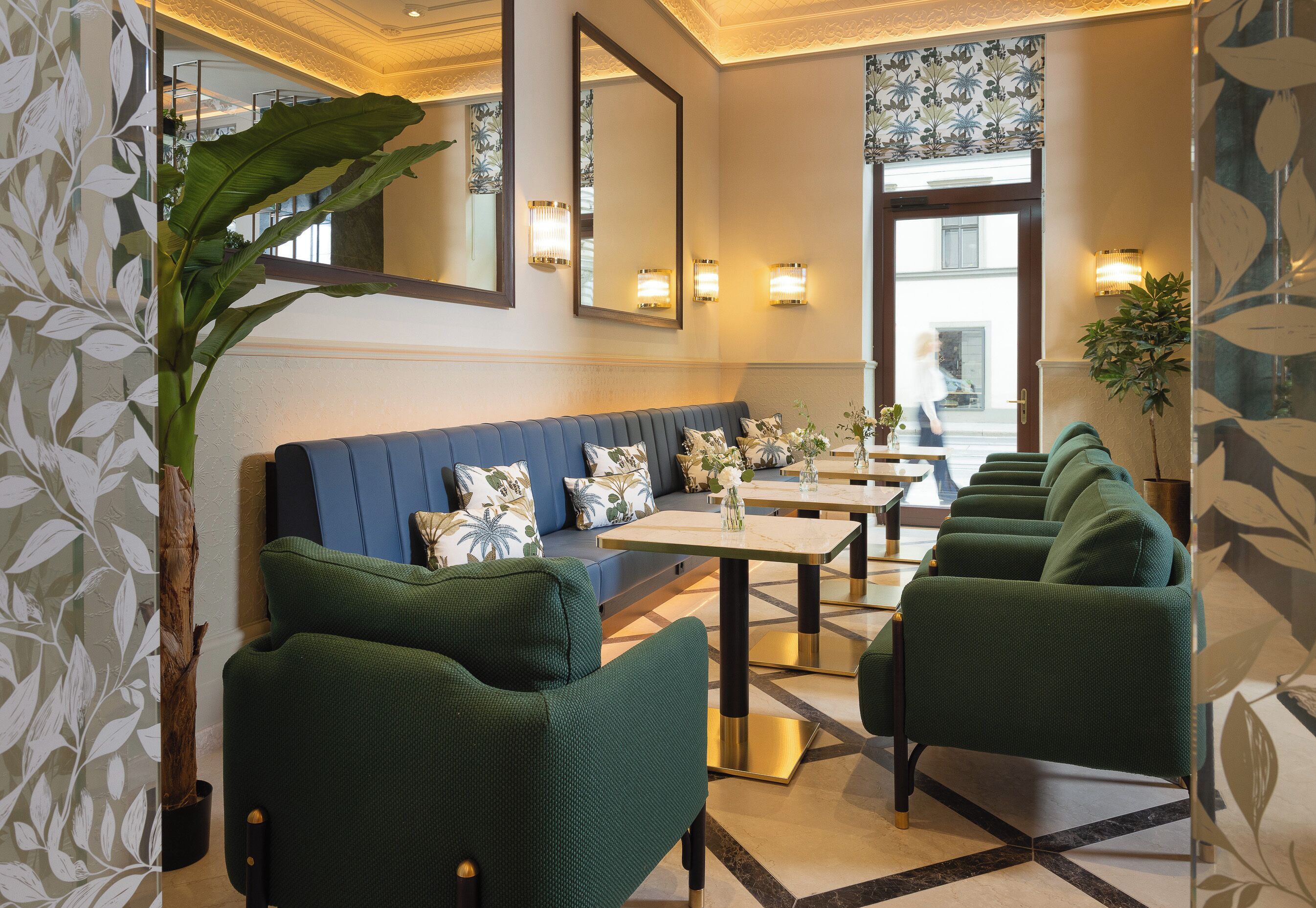 A hotel lobby with a blue sofa, green chairs, a marble coffee table, and a large mirror.