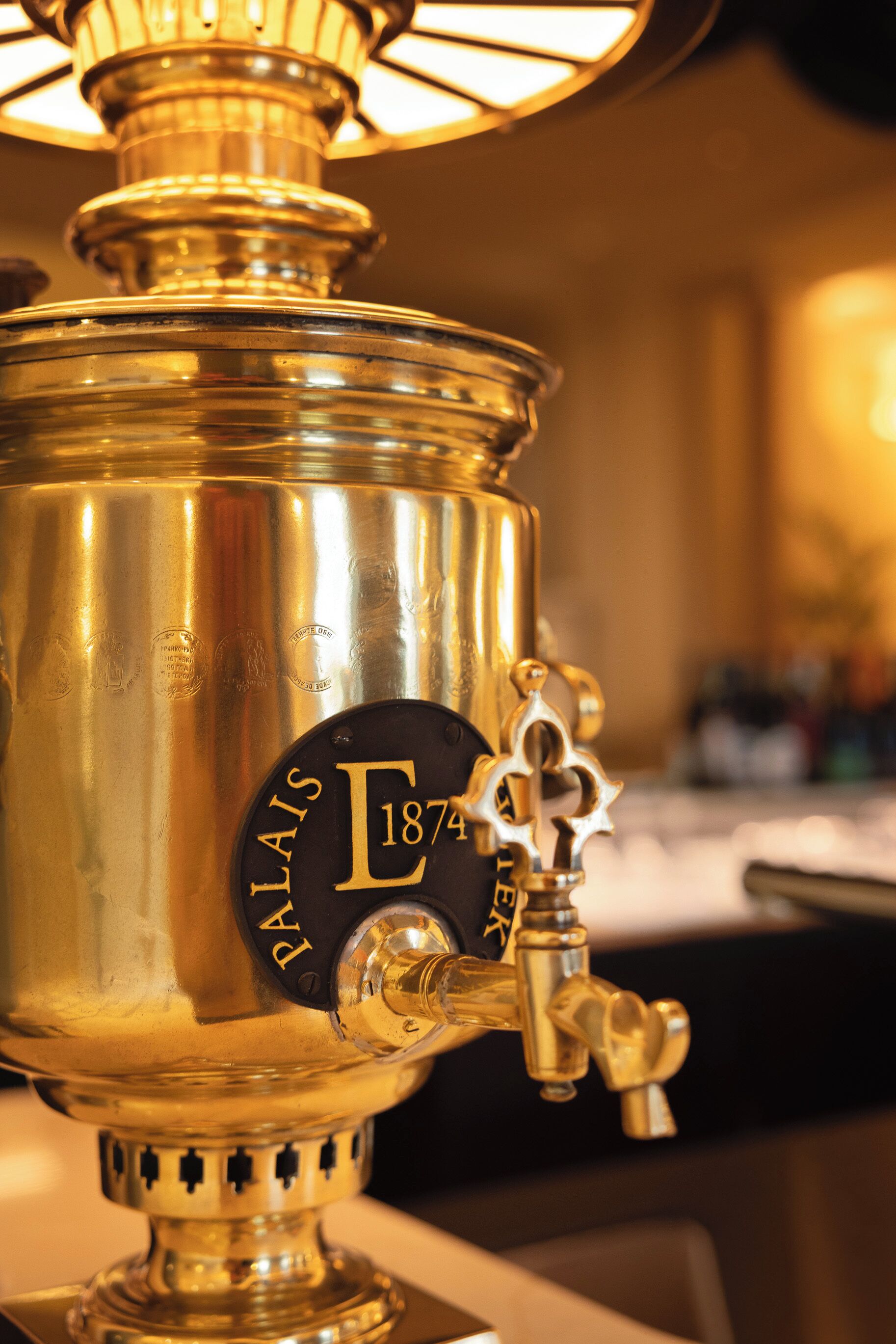 A brass water dispenser with a label reading 'E 1874' and a spigot.