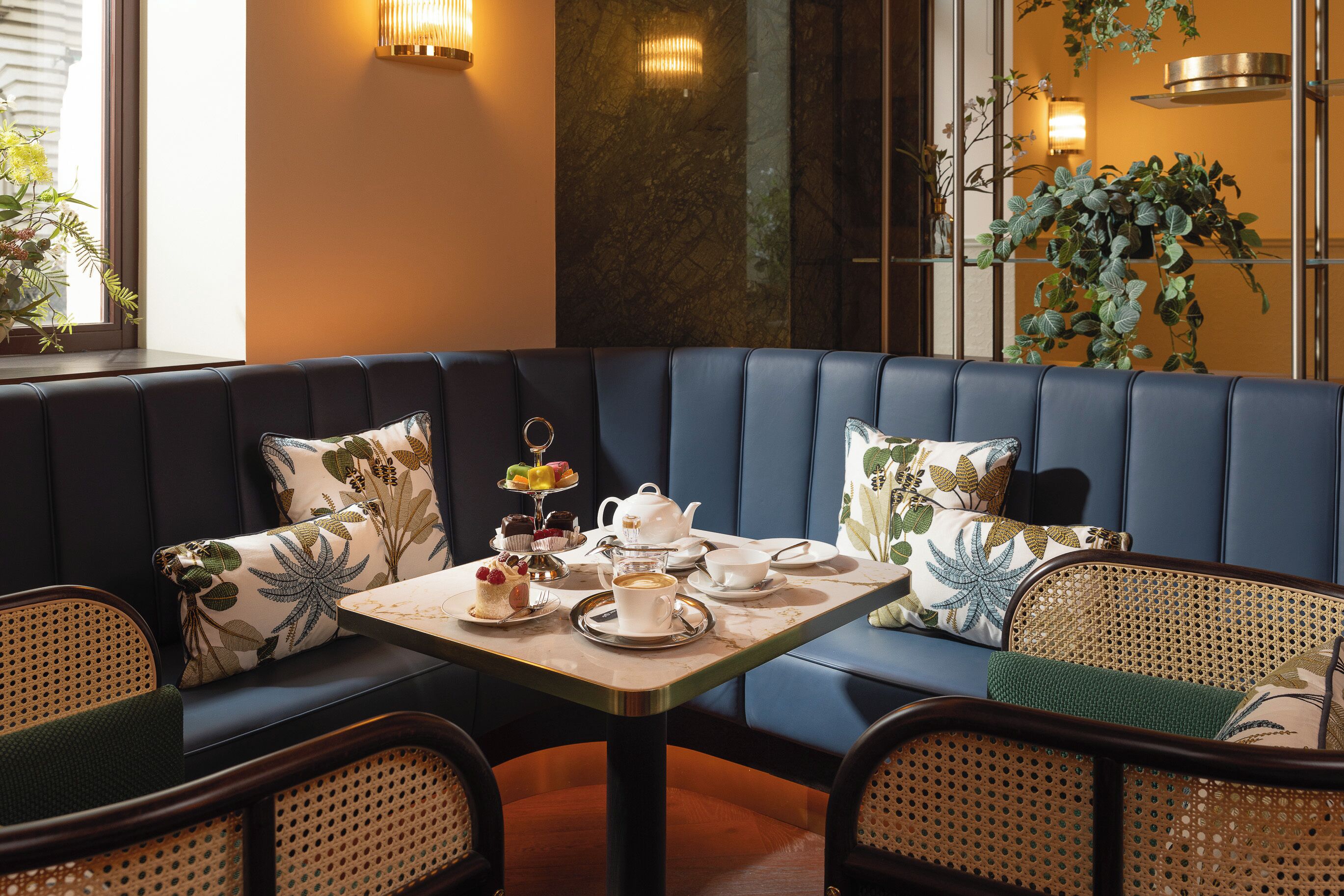 Un rincón con asientos, una mesa dispuesta para el té, un sofá con cojines estampados y una planta en maceta.