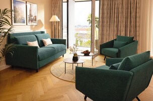 Sala de estar com sofá, poltronas, mesa de centro e vista através de grandes janelas.