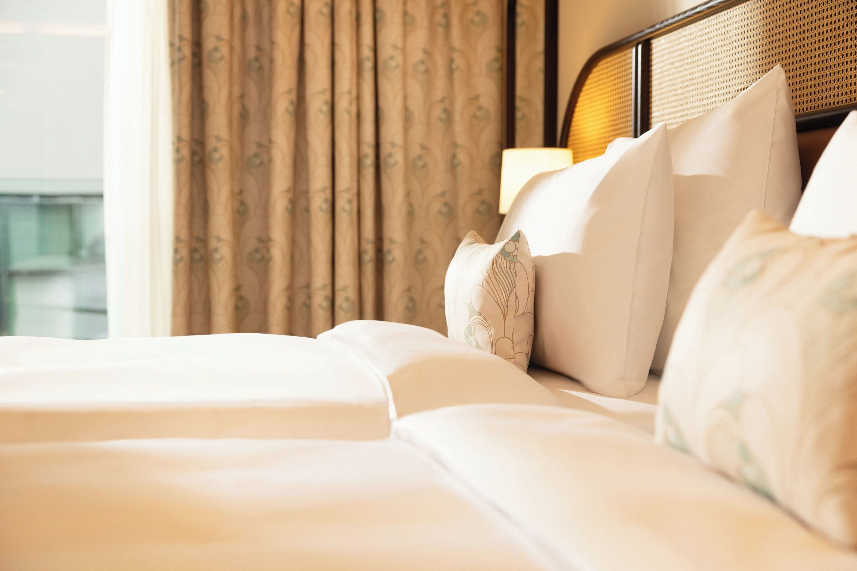 A hotel room with a bed, pillows, and a window with curtains.