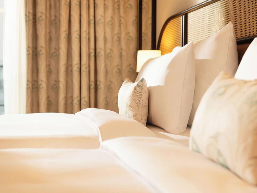 A hotel room with a bed, pillows, and a window with curtains.