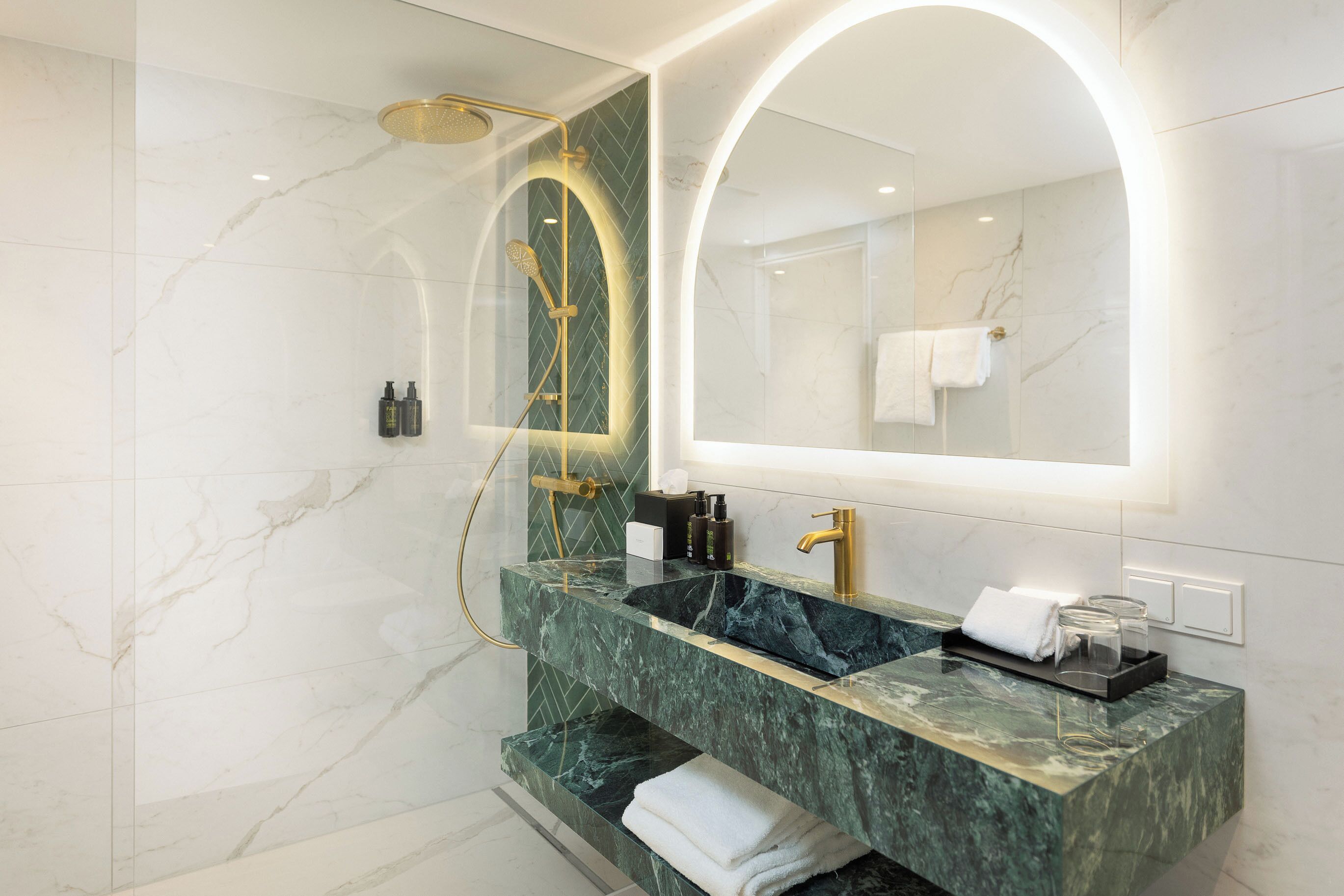 Un baño moderno con tocador de mármol, un espejo grande y una ducha con cabezal dorado.