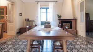 A dining room with a wooden table, chairs, a chandelier, a fireplace, and patterned flooring.