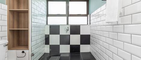 A bathroom with a toilet, a wooden shelf, a black and white tiled shower area, and a window.