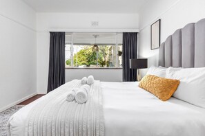 A hotel room with a large bed, a view through a window, and a bedside lamp. - 1 Plomarion (Cape Town)